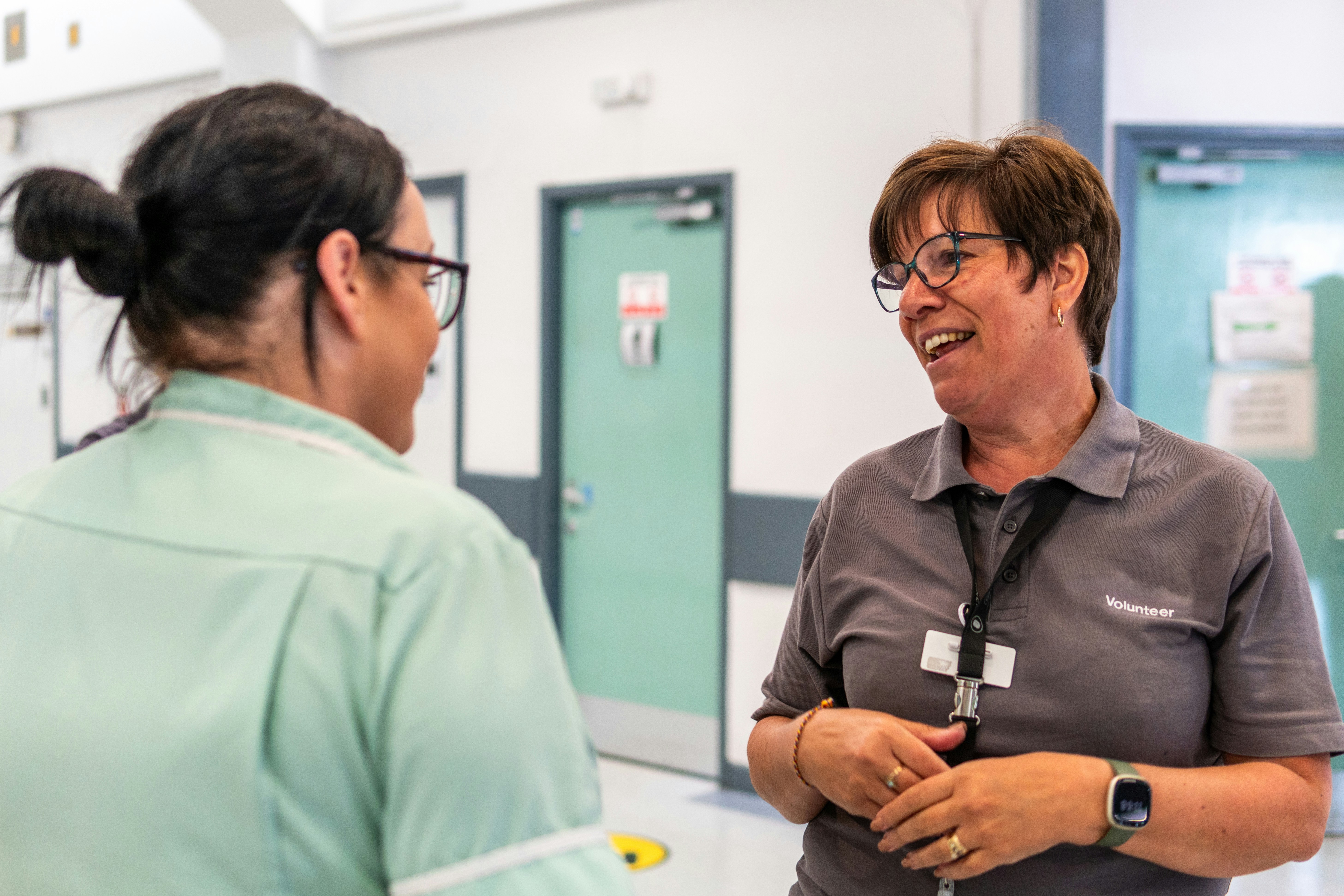Two healthcare staff in conversation in a clinic hallway, both smiling